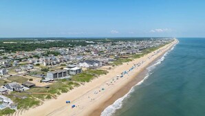 An aerial view of a coastal town with a long beach lined with houses and a clear blue sky. - Gone Coastal | Oceanfront | Community Pool (Kill Devil Hills)