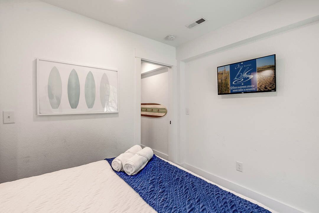 Una camera d'albergo con un letto, un tappeto blu con texture, un'opera d'arte incorniciata e una televisione che mostra una spiaggia.