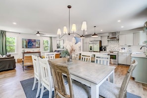 A modern kitchen with white cabinetry, a central island, and a dining area with a wooden table and white chairs.