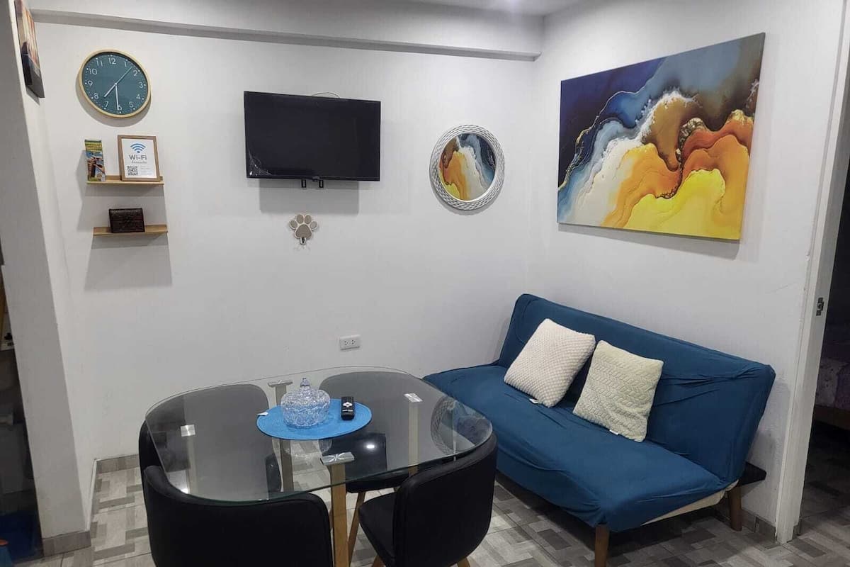 A living room with a glass table, blue sofa, and a painting on the wall.