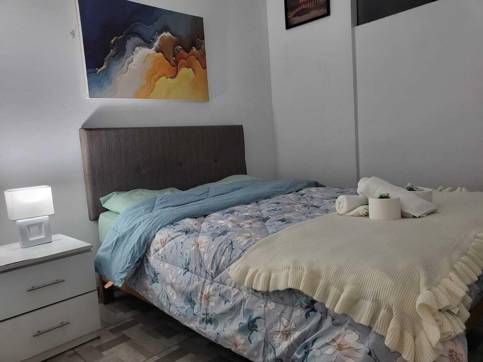 A neatly arranged bedroom with a bed, bedside table, and a painting on the wall.