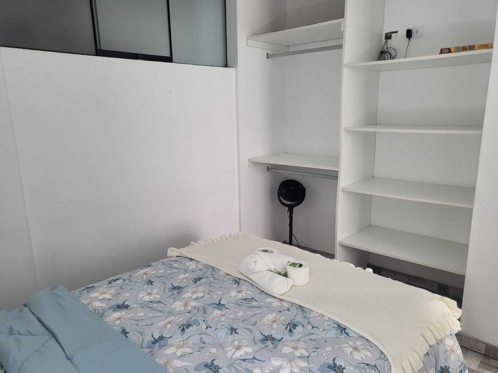 Un dormitorio con una cama, un armario blanco y una mesita redonda con un ventilador.