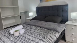 A modern bedroom with a grey striped bedspread, two pillows, a bedside lamp, and a large abstract painting on the wall. - Miel de Luna (Cerro Azul)