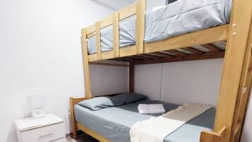 Ein Stockbett mit unterem Bett und Schlafkoje oben, ein Nachttisch mit Lampe und eine kleine Kommode.