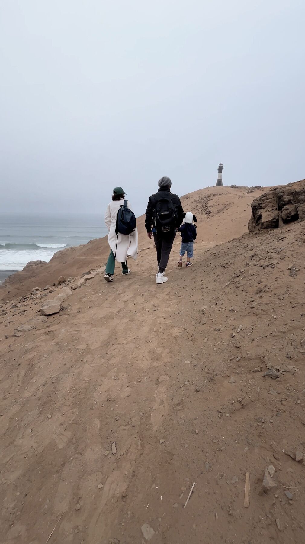 Una playa arenosa con un faro a lo lejos.