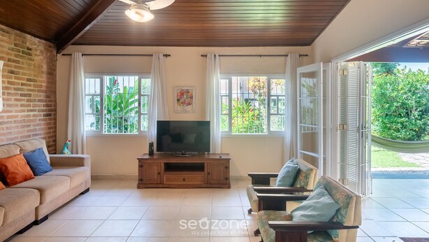 A living room with a wooden ceiling, a TV on a wooden stand, a sofa, and a chair. - House With Barbecue 350m From the Beach Rul0035 (Ubatuba)