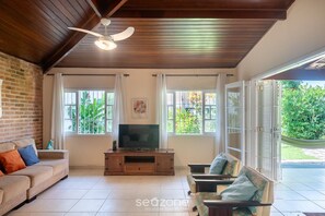 A living room with a wooden ceiling, a TV on a wooden stand, a sofa, and a chair. - House With Barbecue 350m From the Beach Rul0035 (Ubatuba)