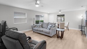 A spacious living room with a grey sofa, a leather chair, a dining table with chairs, and a ceiling fan. - BETTER THAN A 5 STAR HOTEL WITH GOLF CART WHOLE HOUSE TOTALLY REMODELED (The Villages)
