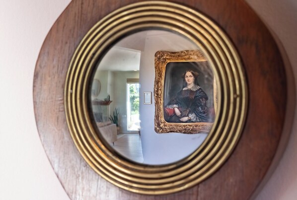 A mirror with a gold frame reflecting a room with a framed portrait and a window. - Completely renovated Mid-Century Modern on Carmel Point - #VR250120 (Carmel)