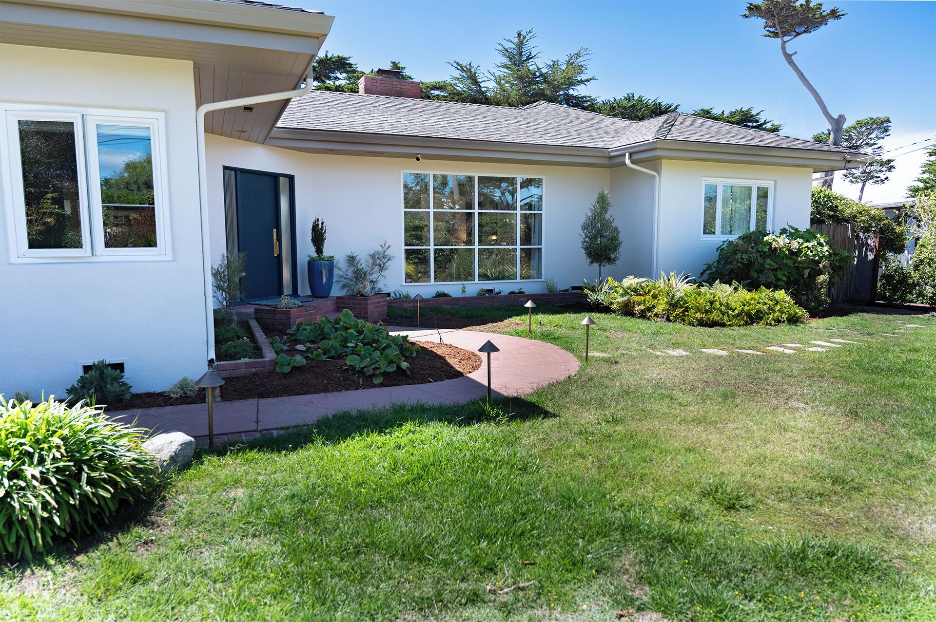 A modern house with a well-maintained lawn, a large window, and a brick pathway leading to the front door.