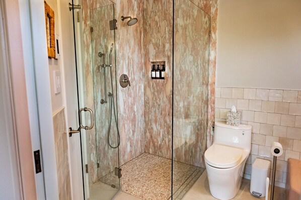 Un baño moderno con ducha de vidrio, inodoro y cubo de basura.