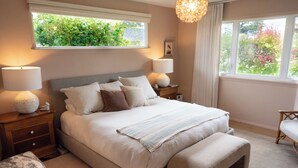 Un dormitorio con una cama grande, dos lámparas de noche, una mesita de noche, una silla y una ventana con vistas a la vegetación.