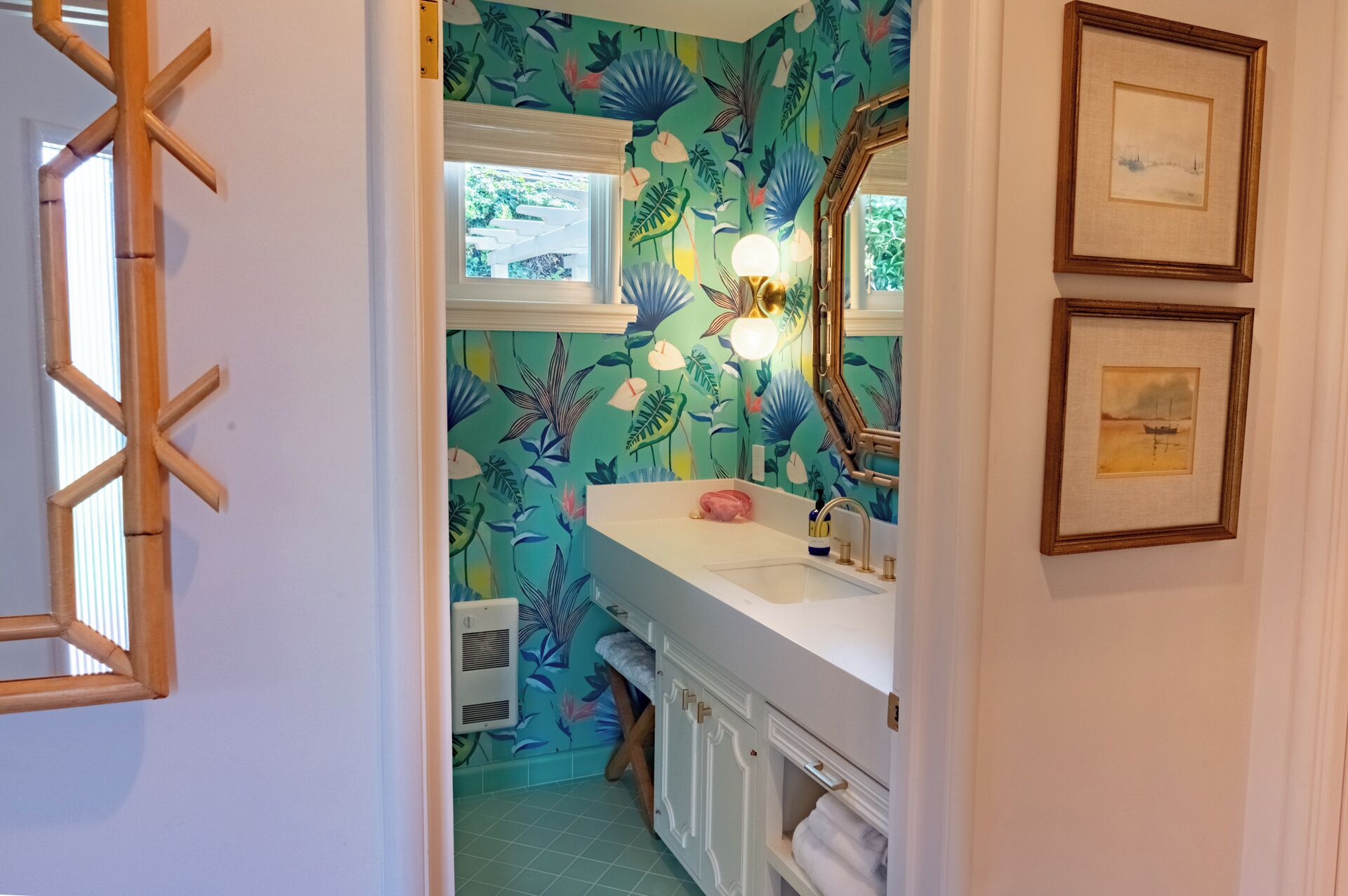 A bathroom with a floral wallpaper, a white sink, a mirror, and a framed picture on the wall.