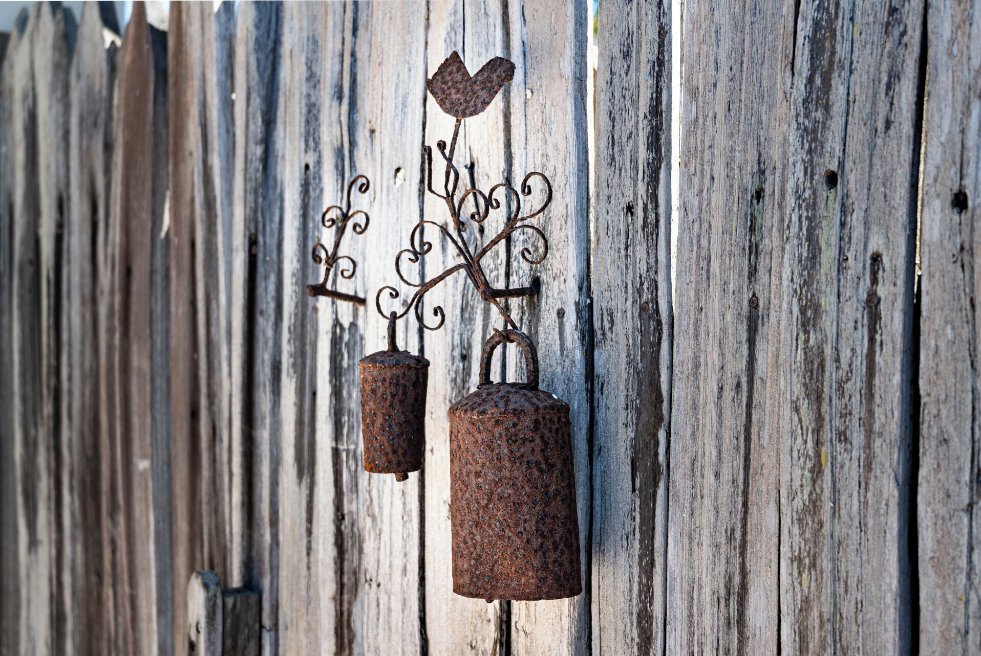 Een rustieke metalen windgong met een hartvormige decoratie en twee cilindervormige belletjes, afgebeeld voor een verweerde houten achtergrond.