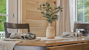 A wooden dining table with a vase of green plants, two chairs, and a woven placemat.