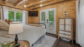 A wooden cabin bedroom with a bed, bedside lamp, dresser, and a TV mounted on the wall.
