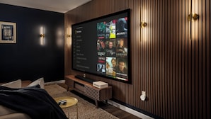 A modern living room with a large flat-screen TV mounted on a wooden wall, a comfortable sofa, and a small coffee table.