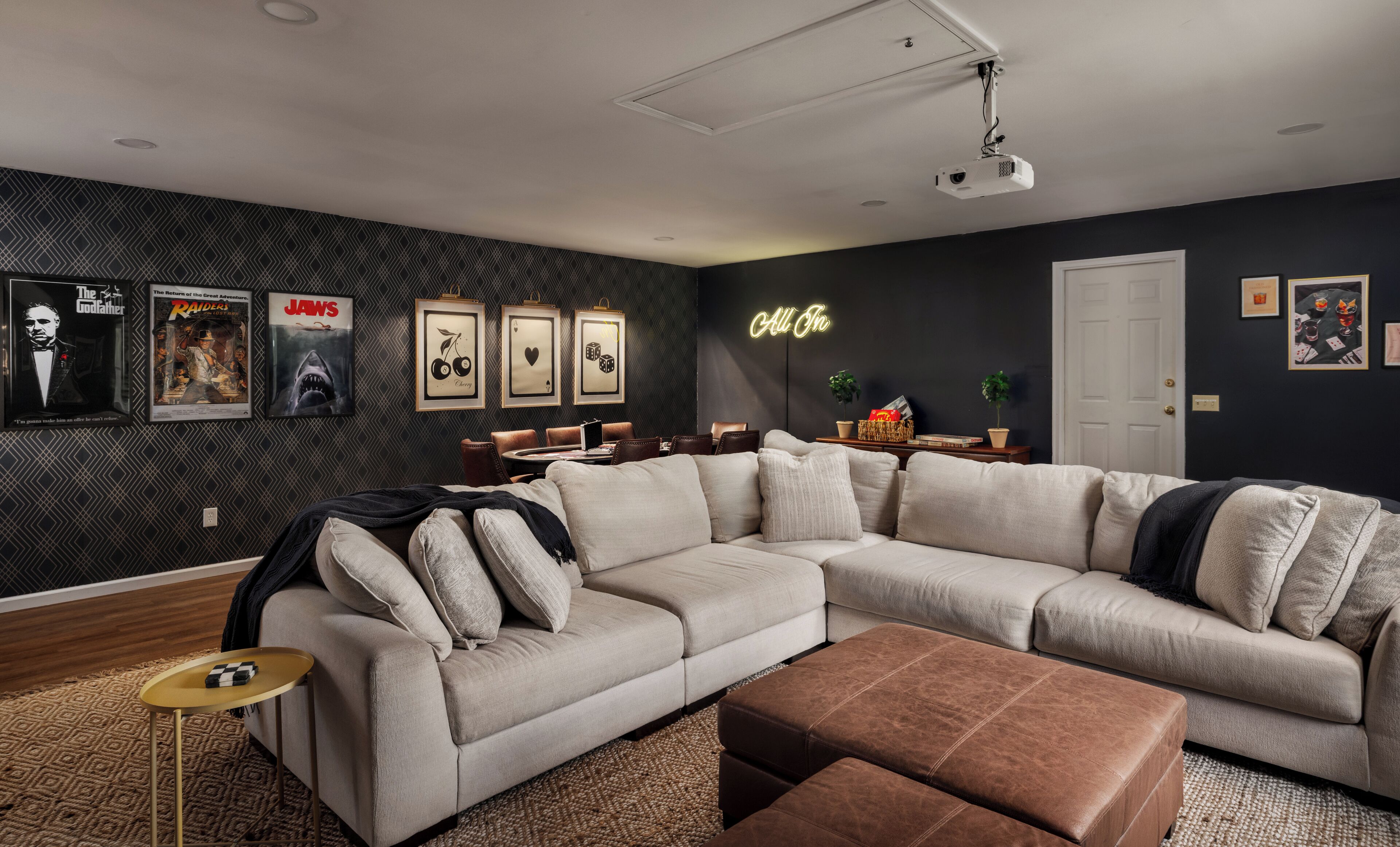 A modern living room with a sectional sofa, a coffee table, and a projector on the ceiling.
