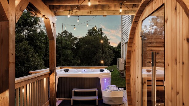 A wooden deck with a hot tub, string lights, and a bench.
