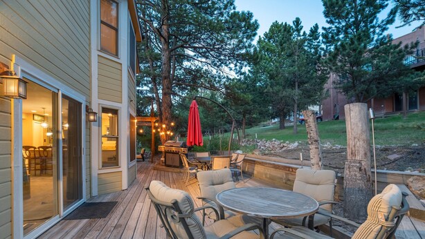Une terrasse en bois avec des meubles d’extérieur, un barbecue et un parasol rouge.
