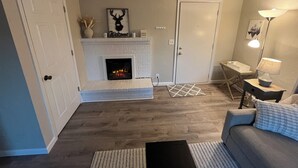 A living room with a fireplace, a sofa, a lamp, and a door. - Charming and relaxing 2-bedroom house in quaint Springfield with AC. Sleeps 6. (Springfield)