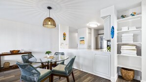 Una cocina moderna con armarios blancos, un comedor con mesa de vidrio y sillas de mimbre, y un techo con lámpara radial.