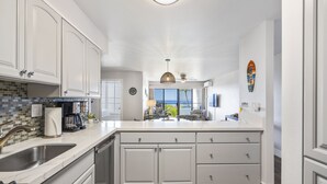 Una cocina con armarios blancos, una isla grande, un fregadero y vista al área de estar.