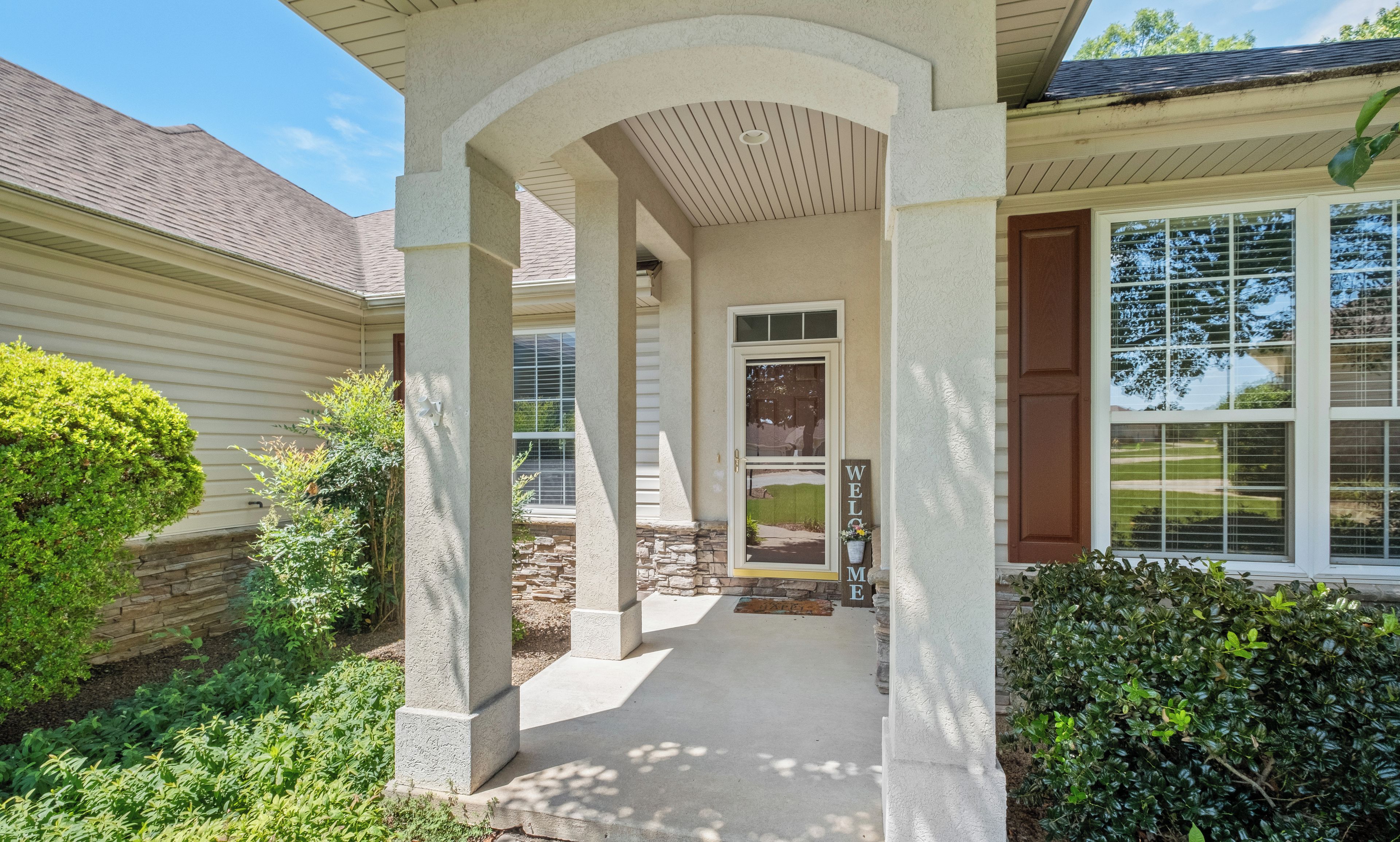 A house with a covered porch, a welcome mat, and a window with blinds.