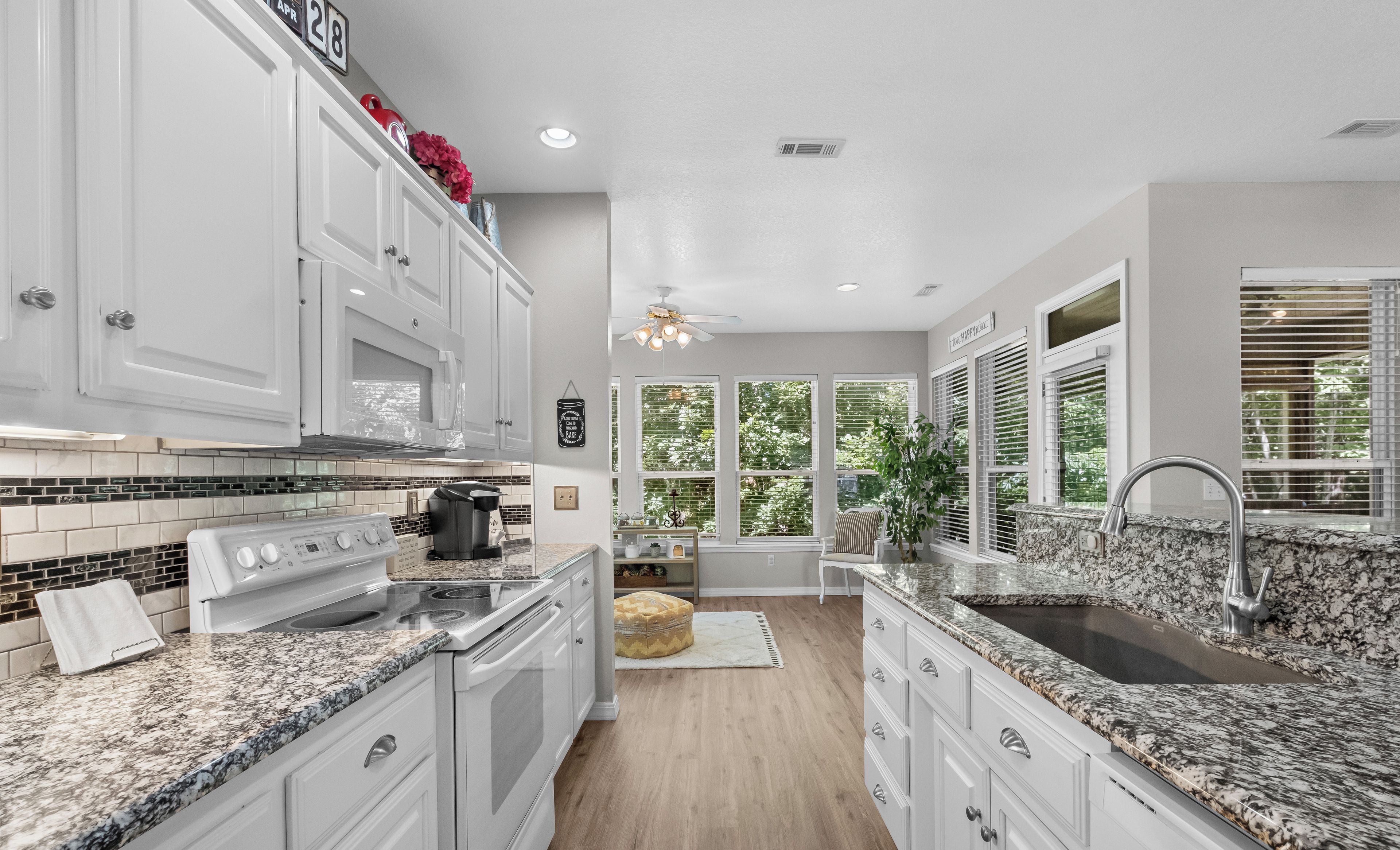 A modern kitchen with white cabinetry, granite countertops, a built-in oven, and a large sink.