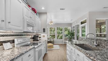 A modern kitchen with white cabinetry, granite countertops, a built-in oven, and a large sink.