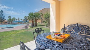 Ein Balkon mit Blick auf einen Pool, ein Tisch mit Obstplatte und ein schmiedeeiserner Stuhl.