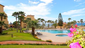 Ein Poolbereich eines Resorts mit Palmen, blauem Himmel und einem Gebäude mit Kuppel im Hintergrund.