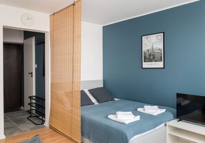 A bedroom with a bed, a TV, a clock, and a cityscape poster.