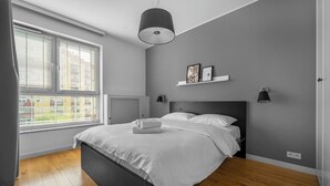 Ein Schlafzimmer mit Bett, Fenster mit Jalousien, Heizkörper und einer Deckenleuchte.
