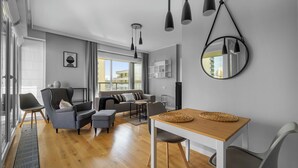 Ein modernes Wohnzimmer mit einer Couch, Sesseln, einem Esstisch und einem großen Fenster.