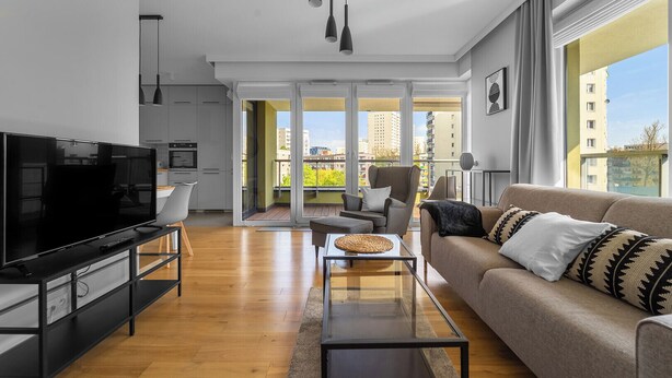 Ein modernes Wohnzimmer mit Flachbildfernseher, einer Couch, einem Couchtisch und einem Balkon mit Blick auf die Stadt.