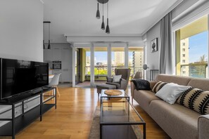 Ein modernes Wohnzimmer mit Flachbildfernseher, einer Couch, einem Couchtisch und einem Balkon mit Blick auf die Stadt.