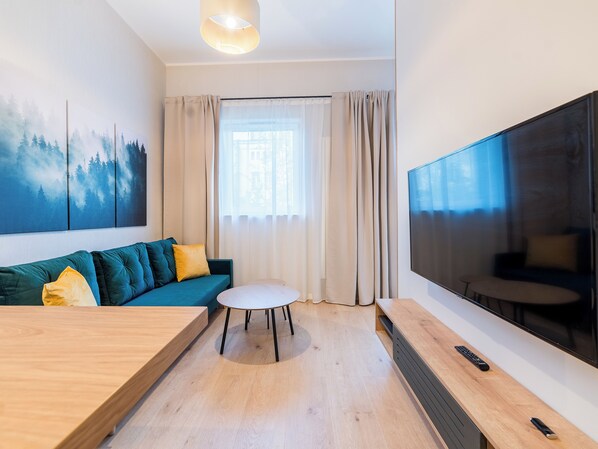 Une chambre d’hôtel moderne, équipée d’un canapé, d’une petite table ronde, d’un grand téléviseur et d’un tableau au mur.