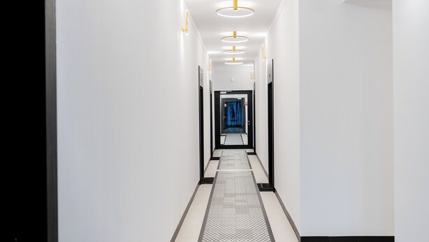 Un couloir moderne et bien éclairé, doté d’un sol à motifs géométriques, qui mène à une porte ornée d’un rideau bleu.