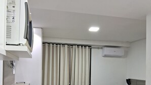 A hotel room with a bed, a desk with a computer, a chair, a small table, and a window with curtains. - Nomar II (Joao Pessoa)