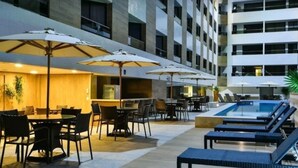 A hotel lobby with a pool area, outdoor seating, and umbrellas. - Nomar II (Joao Pessoa)