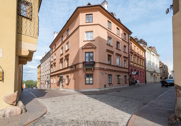A corner building with a cobblestone street, a balcony, and a flag.