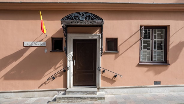 Une entrée d’immeuble avec une porte marron, une enseigne au-dessus de la porte et une fenêtre avec des volets.