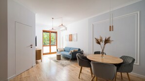 Un salon moderne avec un plancher en bois, un canapé bleu, une table à manger avec des chaises et une grande fenêtre donnant sur un paysage verdoyant.