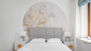Une chambre à coucher moderne avec un grand lit, deux tables de chevet et une grande œuvre d’art circulaire accrochée au mur.