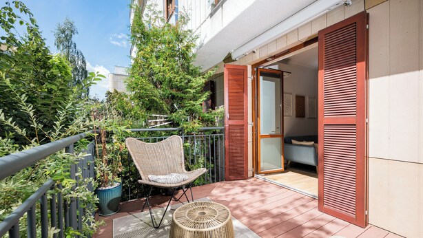Un balcon doté de meubles en osier, d’une plante en pot et d’une porte-fenêtre coulissante donnant sur une pièce.