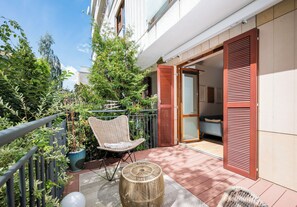 Een balkon met rieten meubilair, een bloempot en een schuifdeur naar een kamer.