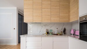 Une cuisine moderne avec des meubles blancs, un pare-feu en marbre et des panneaux de plafond en bois.