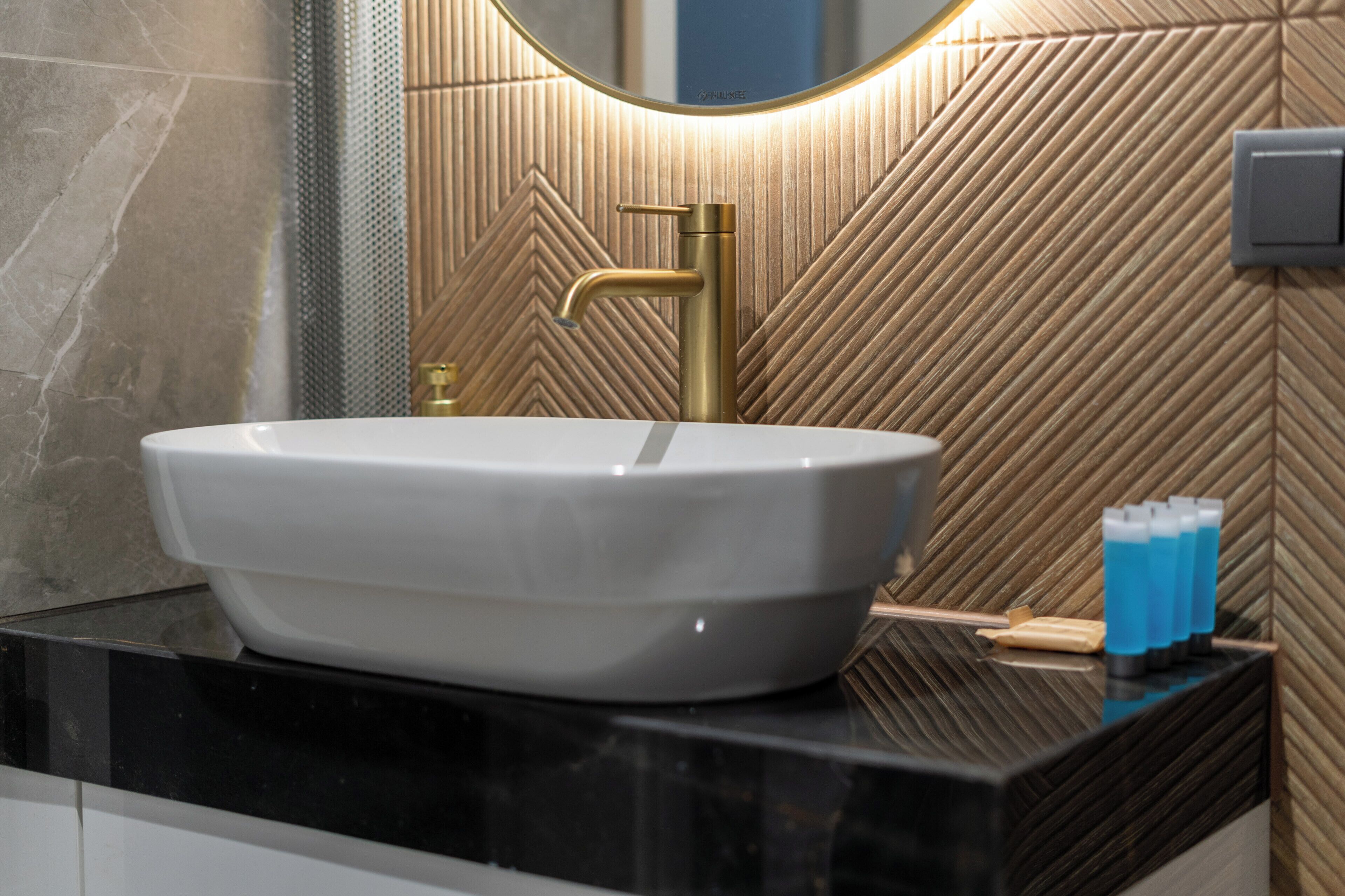 A bathroom with a white sink, gold faucet, and a mirror with a wooden wall design.