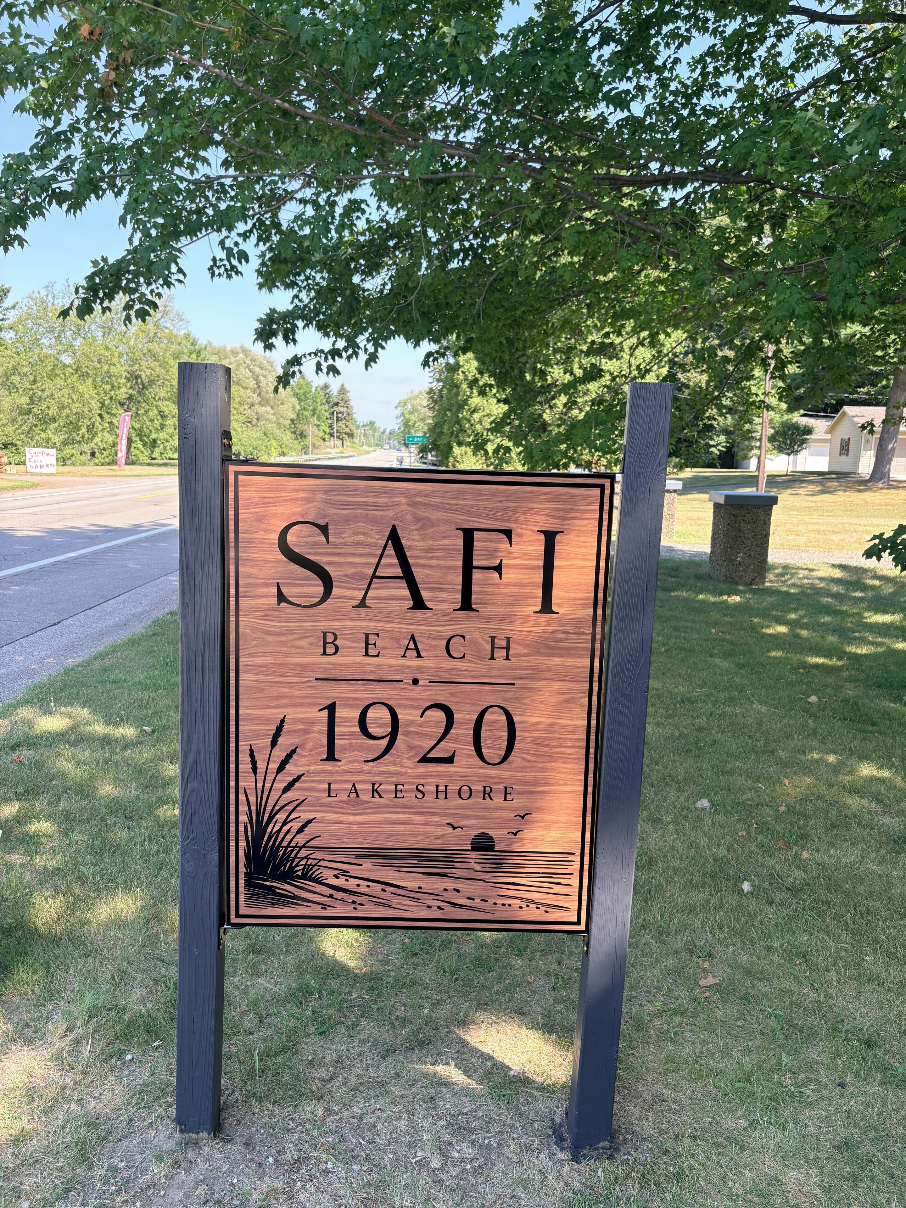 A wooden signboard with the text 'SAFI BEACH 1920 LAKESHORE' mounted on two poles.
